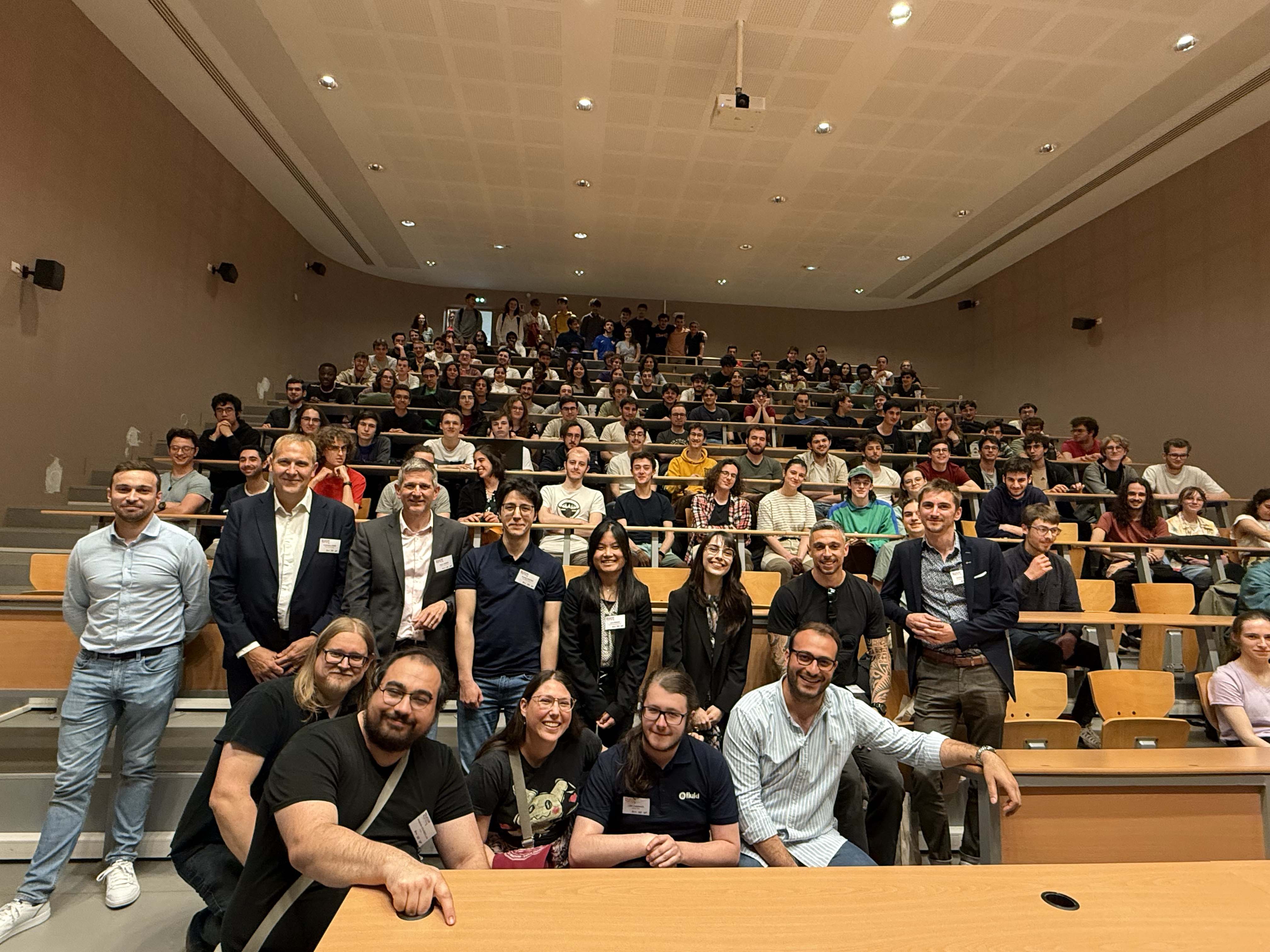 Un groupe de 13 diplômés devant un amphithéâtre rempli d'élèves