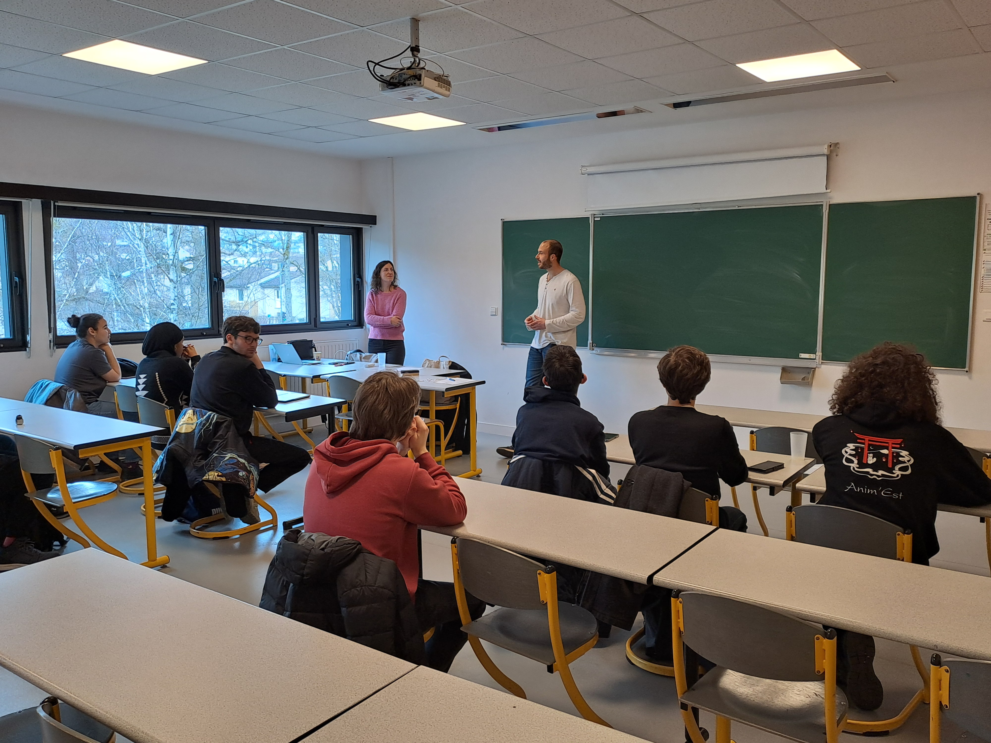 Un groupe de 7 étudiants sont assis dans une salle de cours et écoute un couple d'intervenants